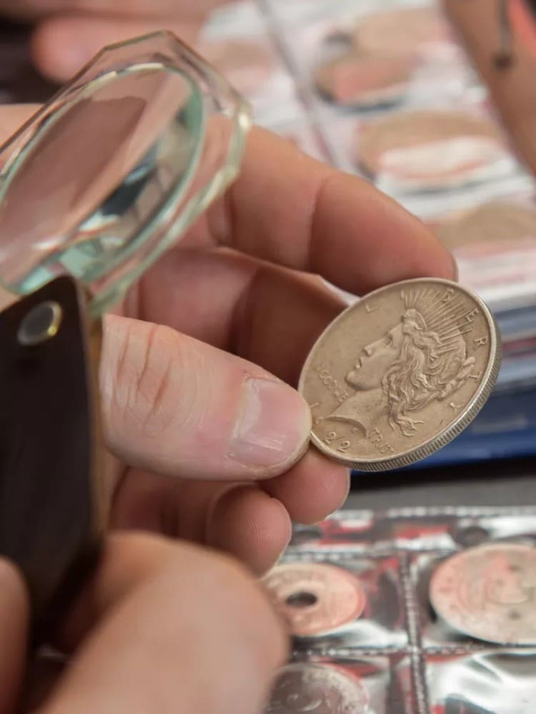 Numismatist in the process of inspecting the quality and engravings of coins using a handheld magnifying glass.