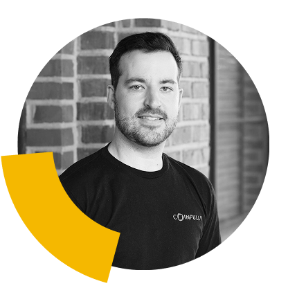 Cooper Sitton, a man with a beard, wearing a black Coinfully t-shirt, against a brick wall background.