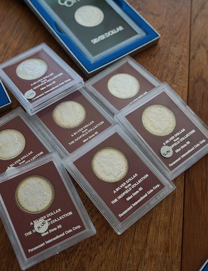 Collection of silver dollar coins in protective cases, with a blue box in the background.