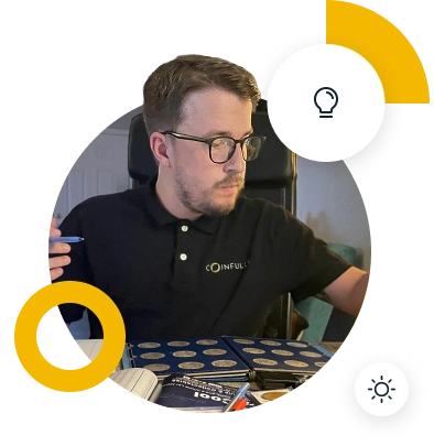 A person wearing a black Coinfully polo shirt is seated at a desk with various items, looking at a notebook.