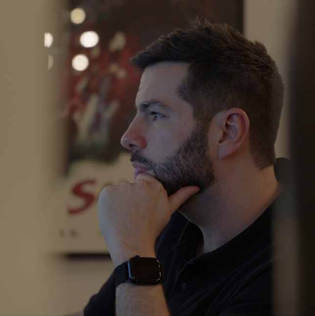 A man with a beard rests his chin on his hand while focused on a computer screen.