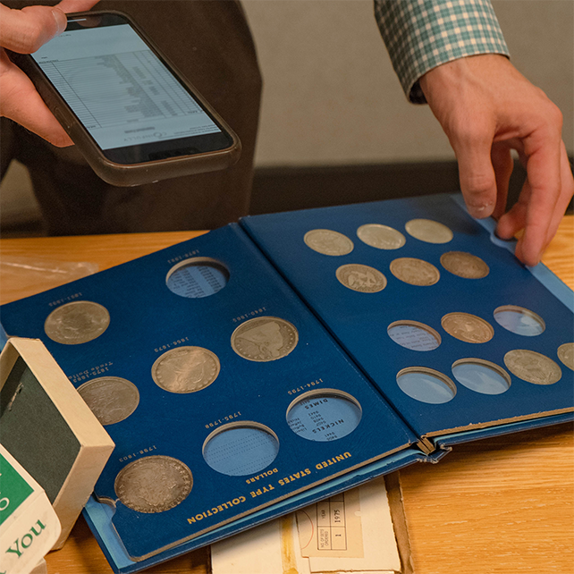 Reviewing a blue coin album with various coins while holding a smartphone.