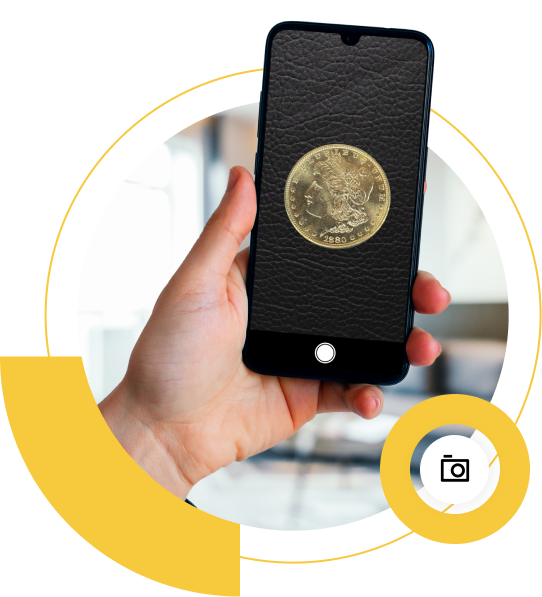 A hand holding a smartphone displaying a gold coin on a black background, with a blurred interior in the background.